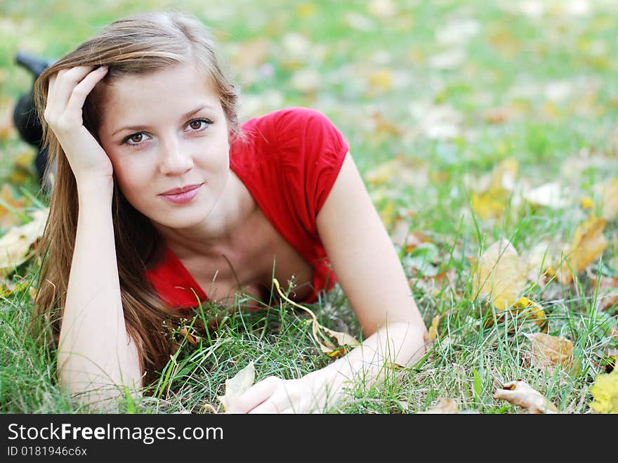 Young beautiful woman lying on the green grass with maple leaf. Young beautiful woman lying on the green grass with maple leaf