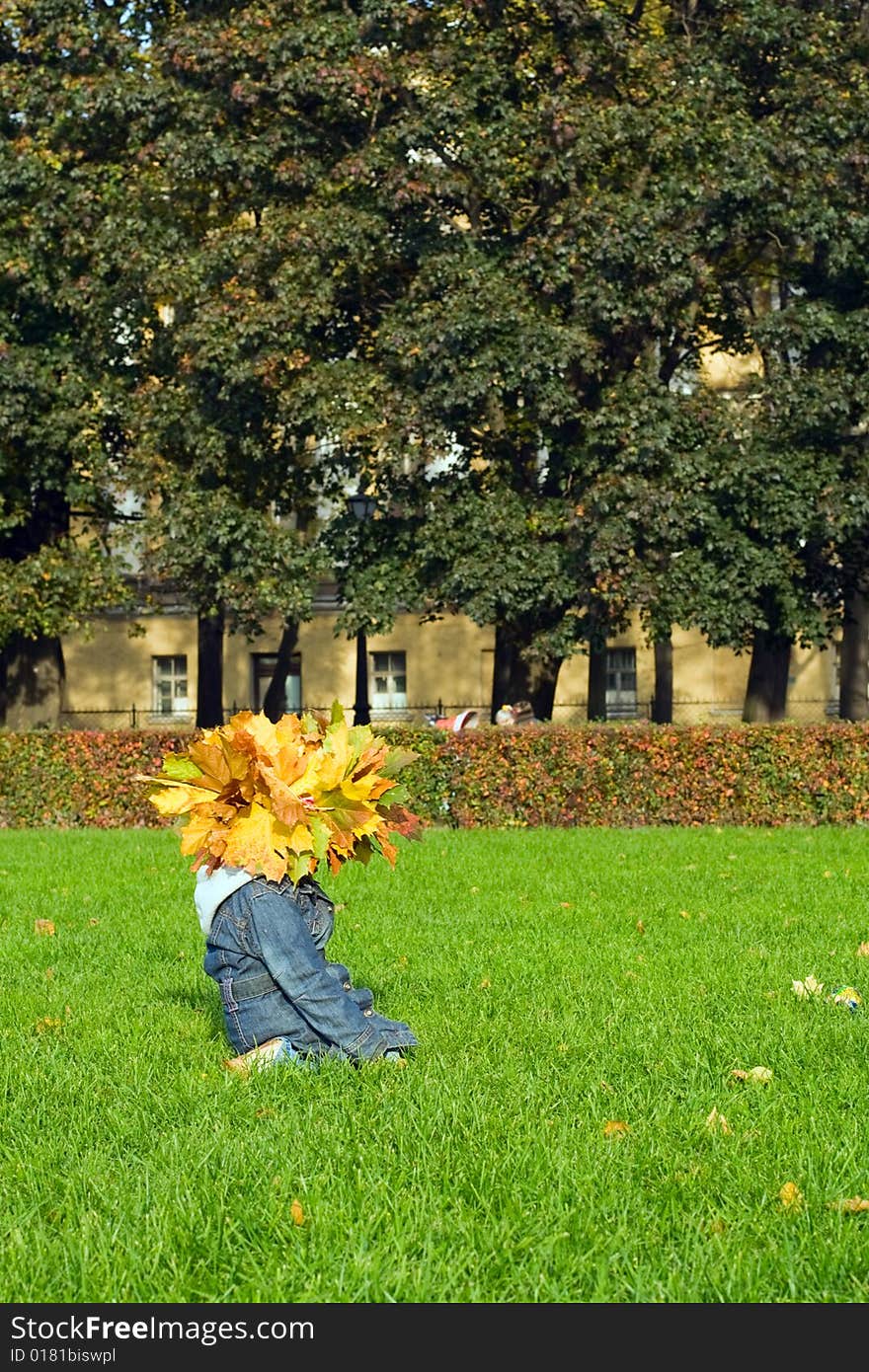 Little girl at maple yellow leaves on her head. Seats at green grass. Little girl at maple yellow leaves on her head. Seats at green grass.