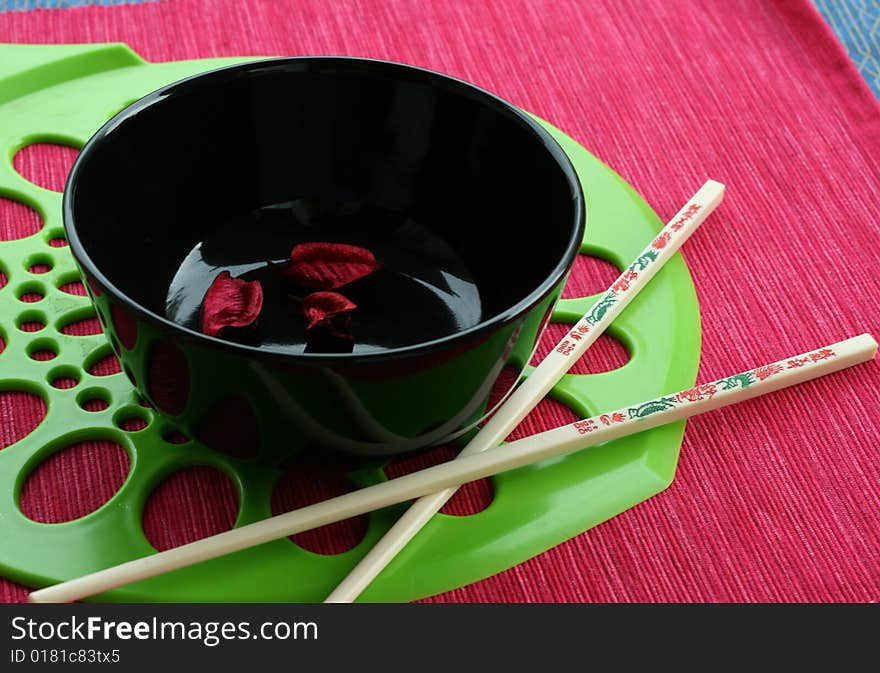 Black bowl and the Chinese sticks on a red-green background