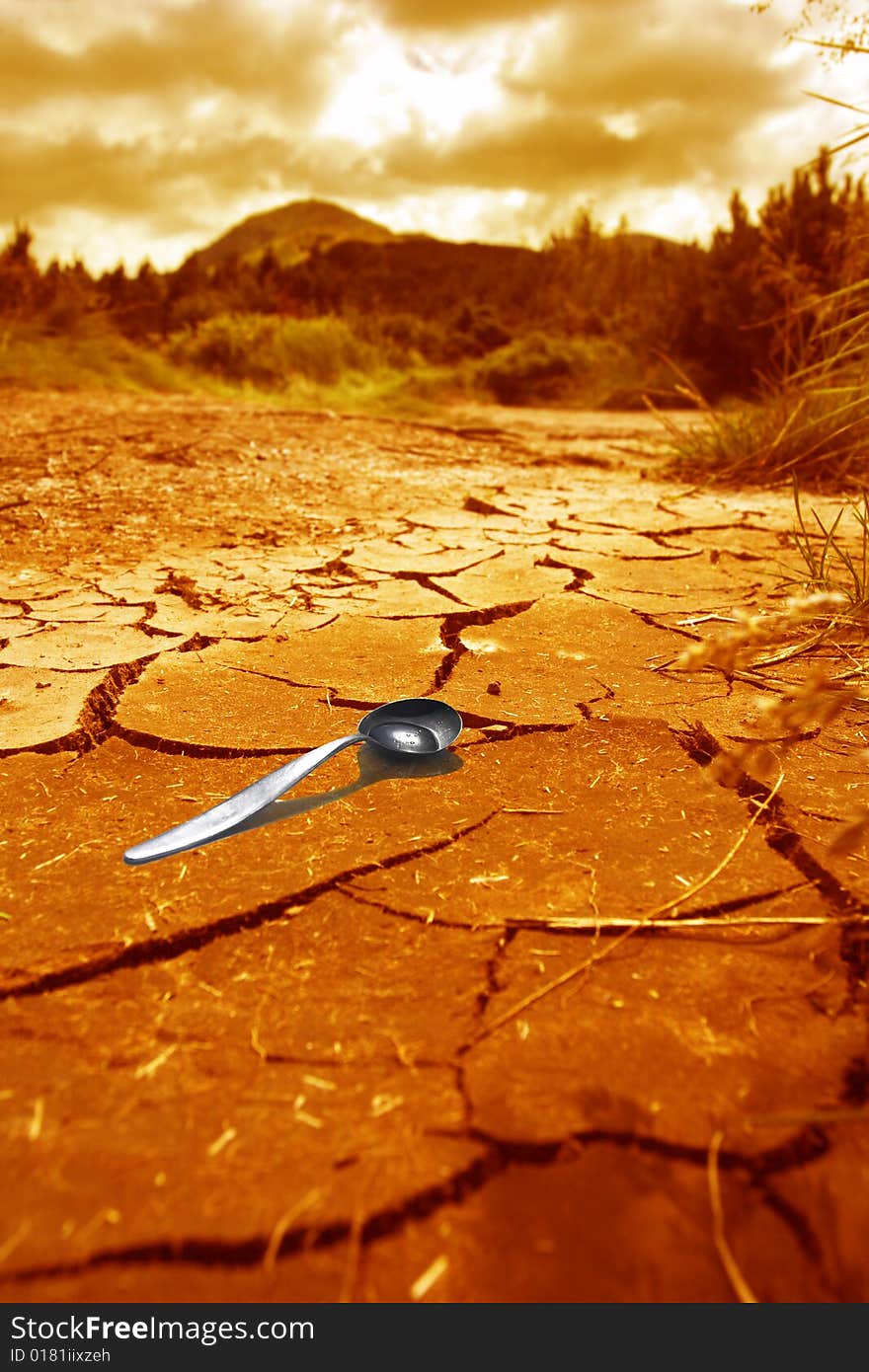 The spoon with a small water drop lying on the dry soil. The spoon with a small water drop lying on the dry soil