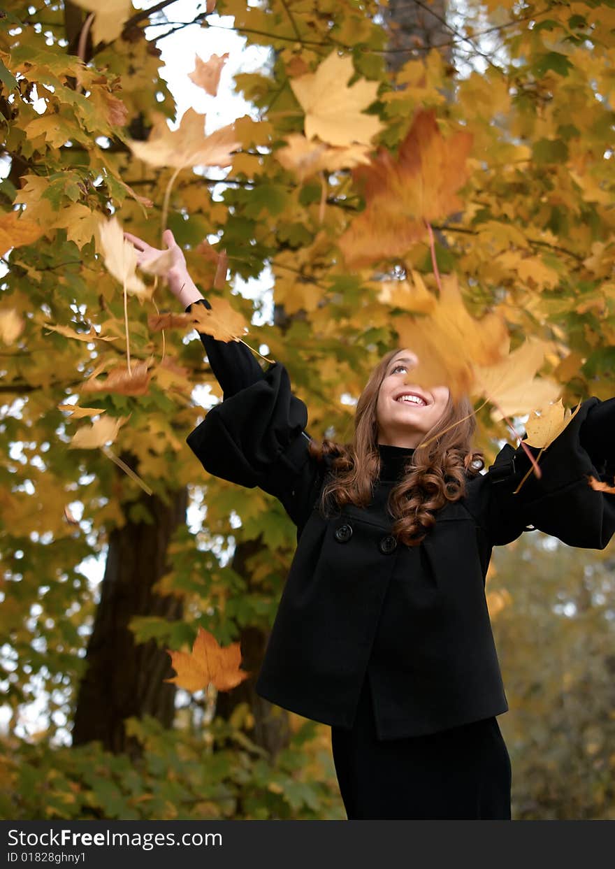 Youn girl throws leaves upwards in forest.