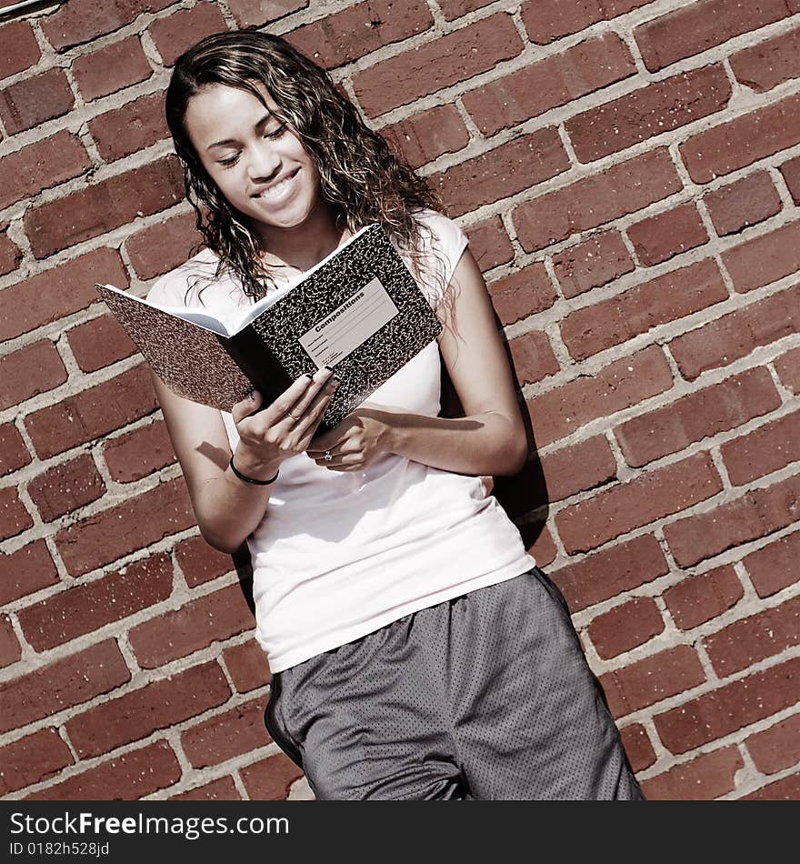 Beautiful young girl reading notebook against a brick wall. Beautiful young girl reading notebook against a brick wall.