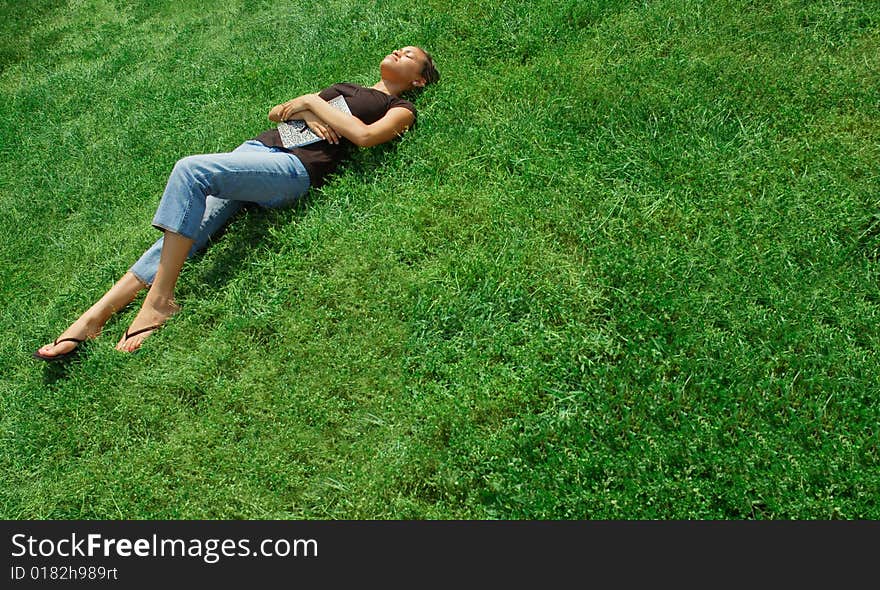 Beautiful young woman laying in green field with notebook. Beautiful young woman laying in green field with notebook.