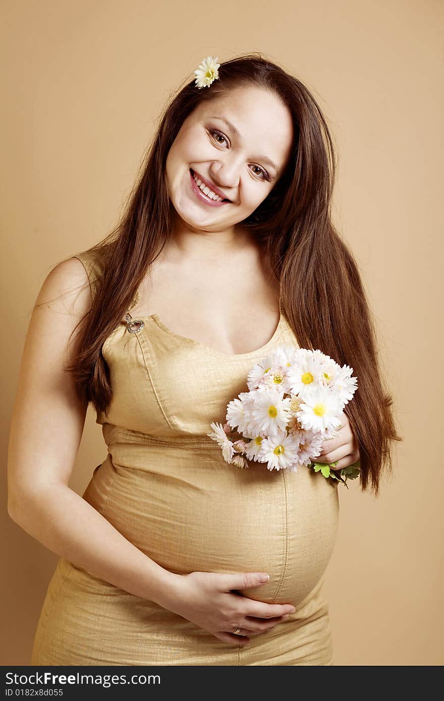 Happy pregnant woman with bouquet of flowers on beige studio background