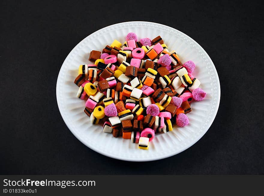 Colorful candy mix on white plate against black background