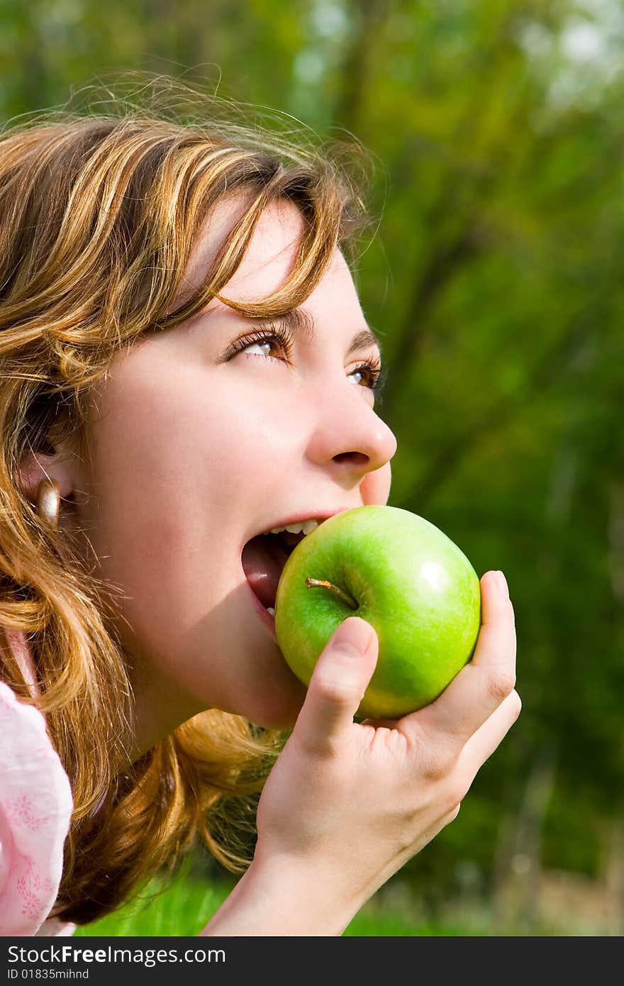 Pretty woman eating green apple on the summer glade