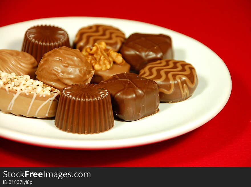 Assorted chocolates on white plate against red background