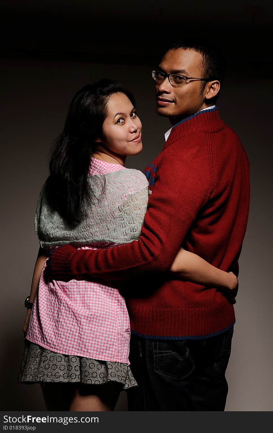 Couple hugging looking backwards smiling on a plain background