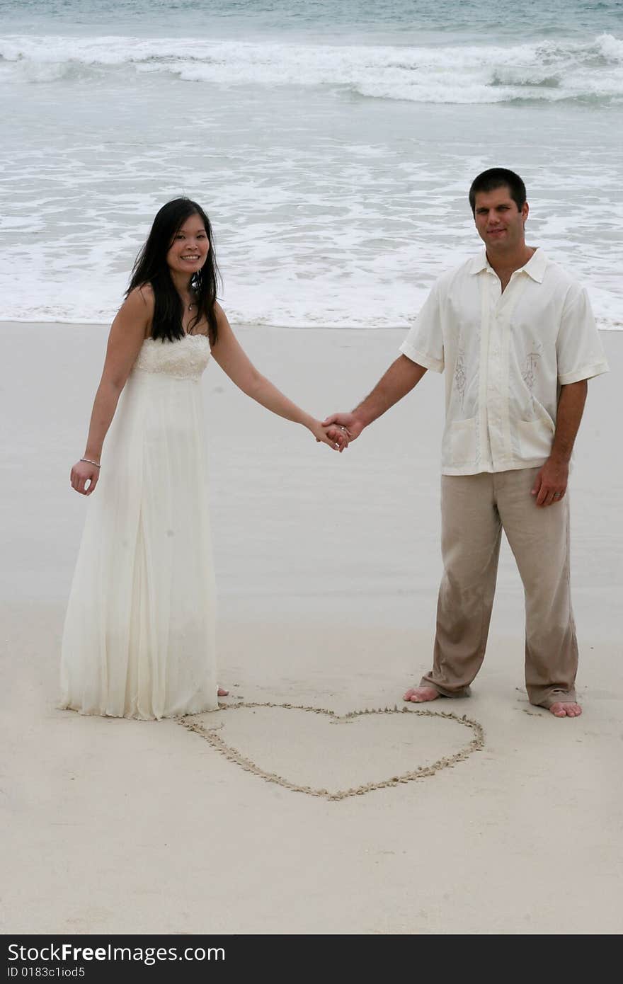 Heart in the sand with bride and groom holding hands. Heart in the sand with bride and groom holding hands.