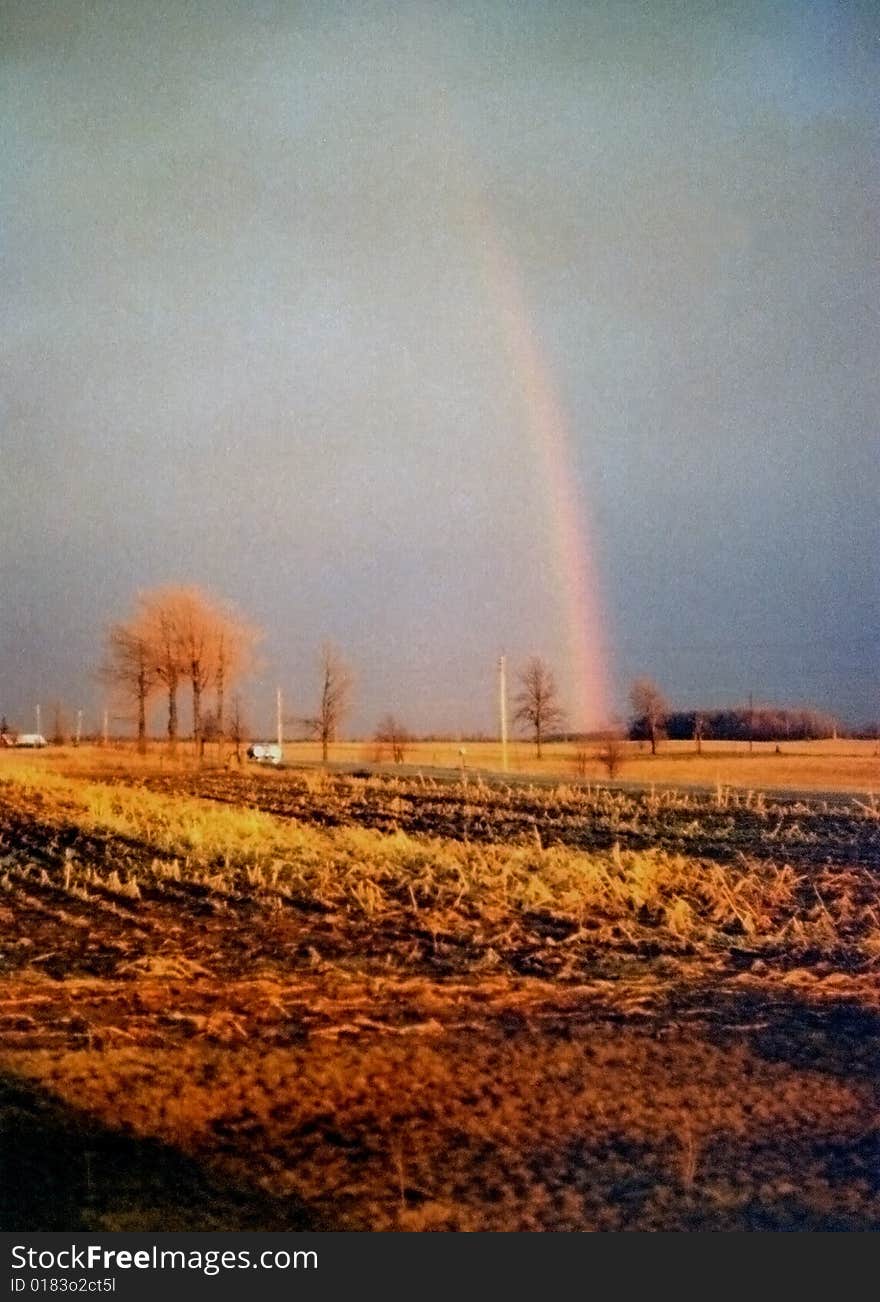 Autumn rainbow after a storm and car with lights on traveling down a country road.