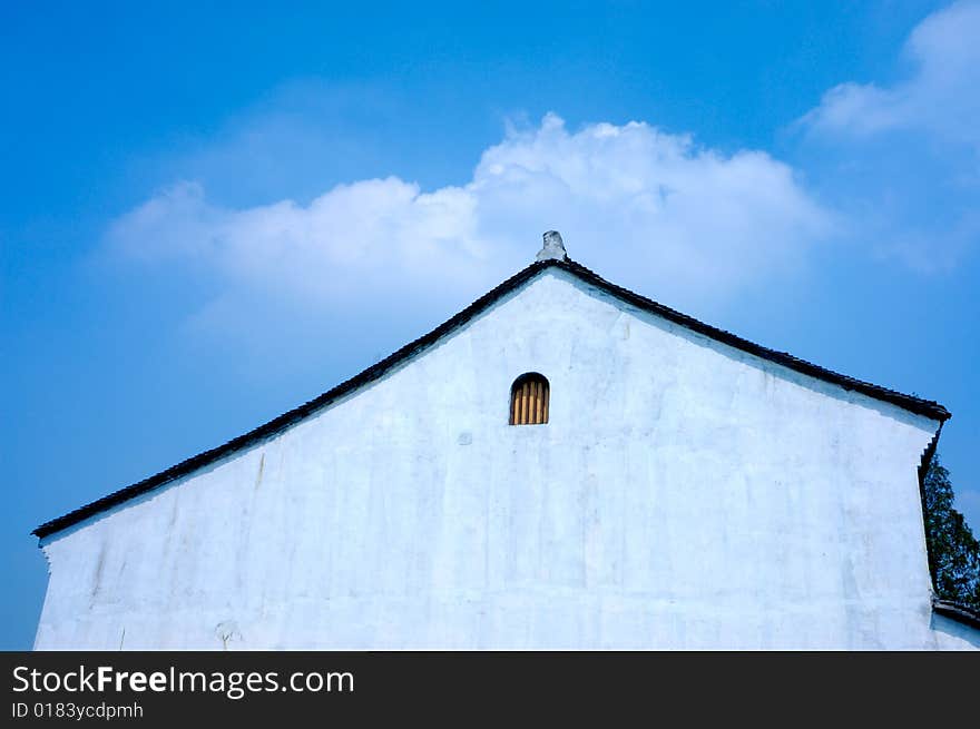 A white wall of a chinese traditional room with a little window under blue sky and white cloud. A white wall of a chinese traditional room with a little window under blue sky and white cloud.