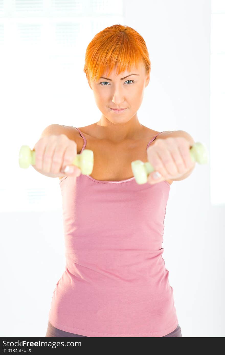 Young woman doing fitness exercise with dumbbells. She's looking at camera. Front view. Young woman doing fitness exercise with dumbbells. She's looking at camera. Front view.