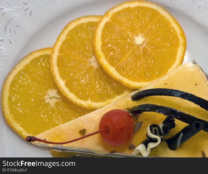 Piece of cake with cherry and three oranges on the dish