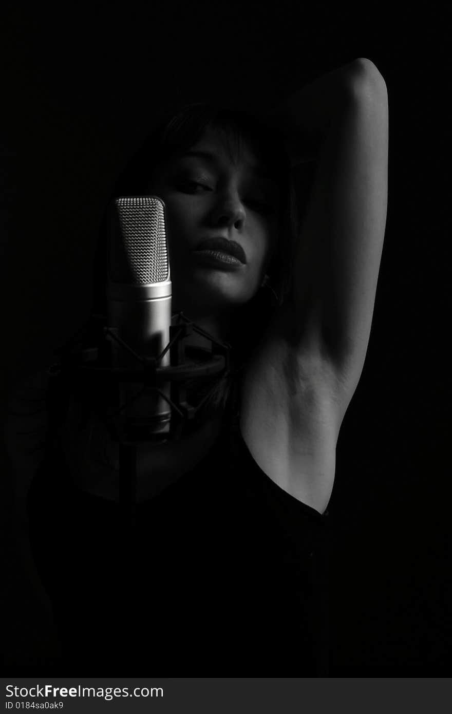 Young woman appears from the darkness behind the microphone. Young woman appears from the darkness behind the microphone