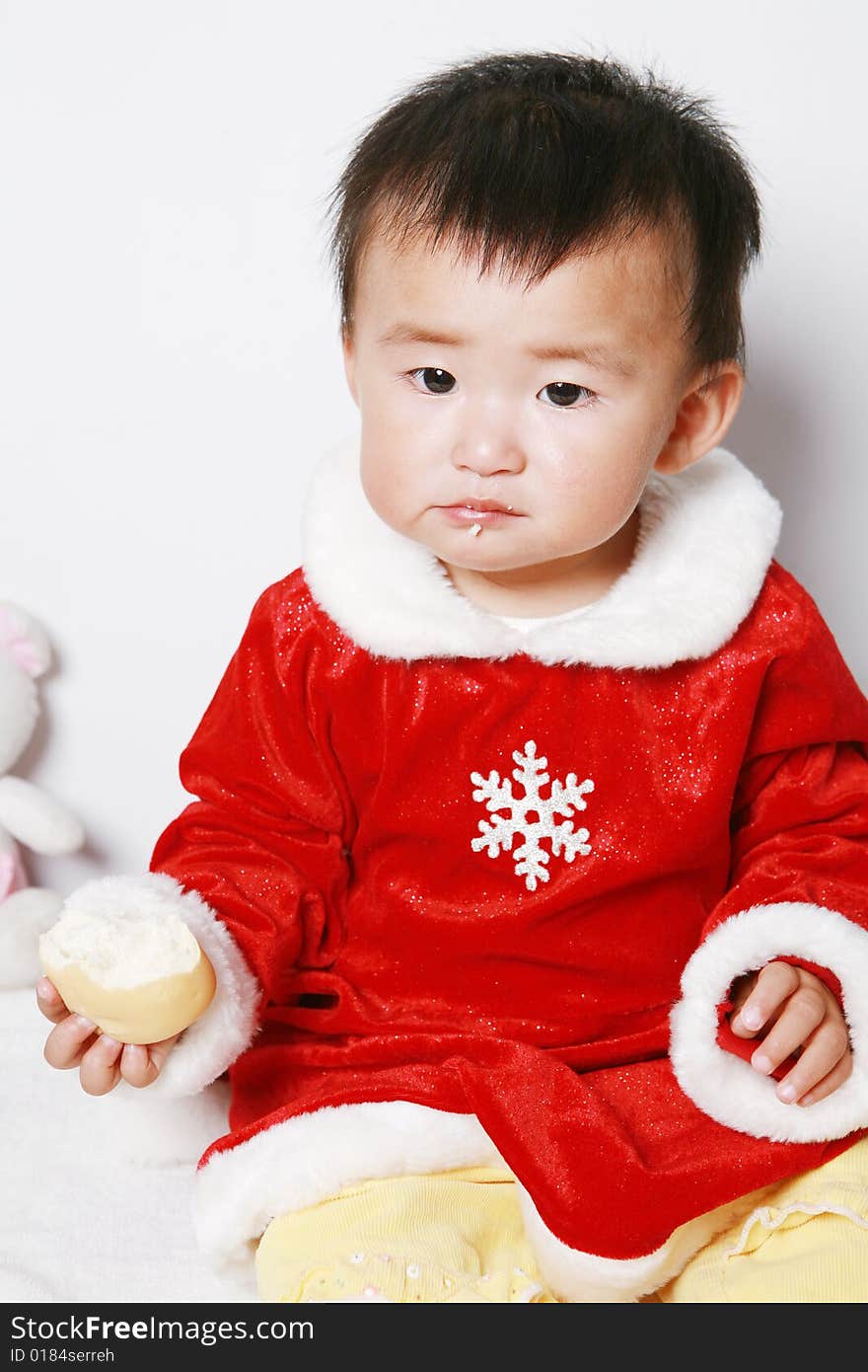 Santa baby in red dress eating a snack.