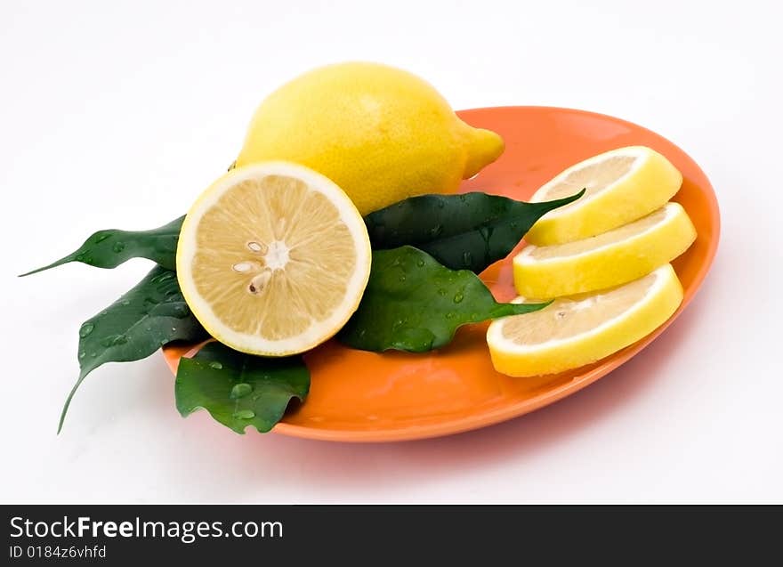 Lemon with green leaves on the orange plate. Lemon with green leaves on the orange plate