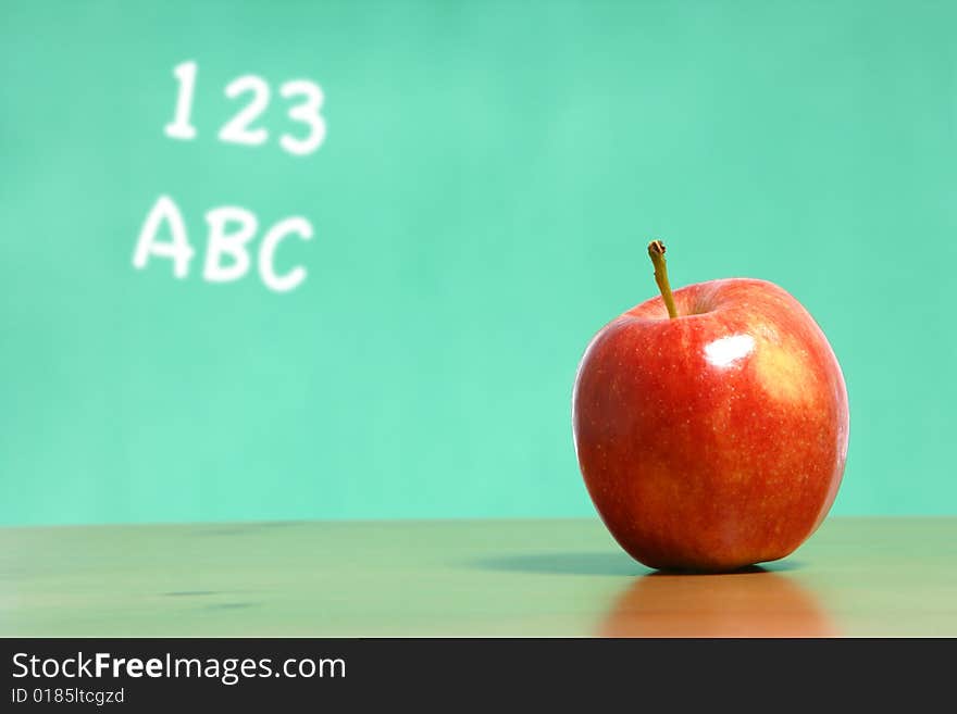 An apple on a desk in a classroom with 123 abc