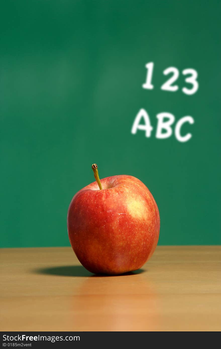 An apple on a desk in a classroom with 123 abc