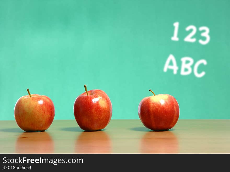 An apple on a desk in a classroom with 123 abc