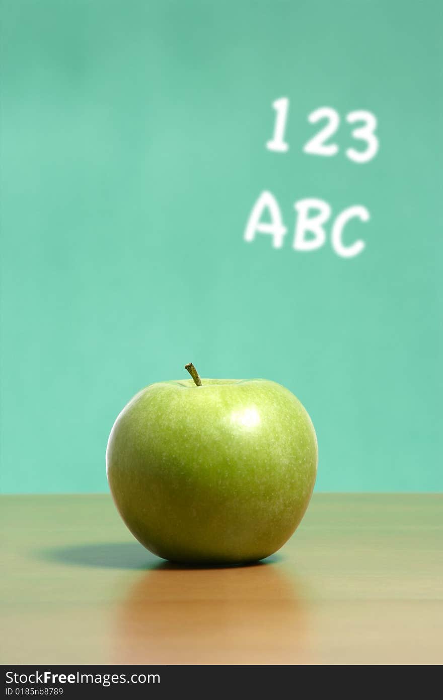 An apple on a desk in a classroom with 123 abc