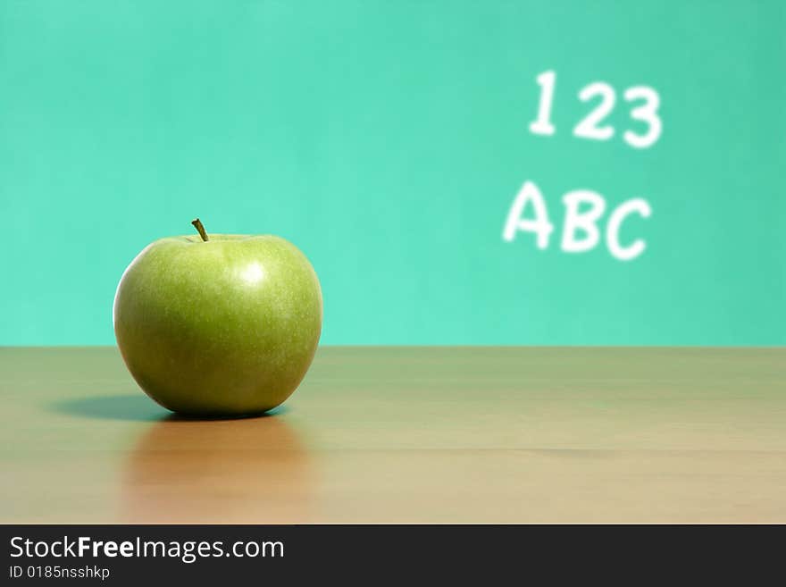 An apple on a desk in a classroom with 123 abc