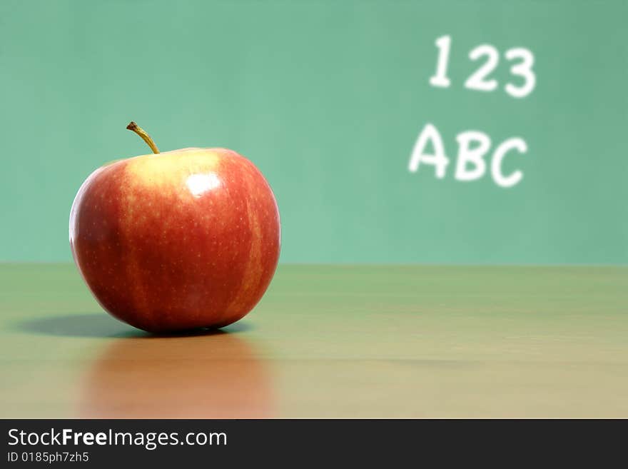 An apple on a desk in a classroom with abc 123