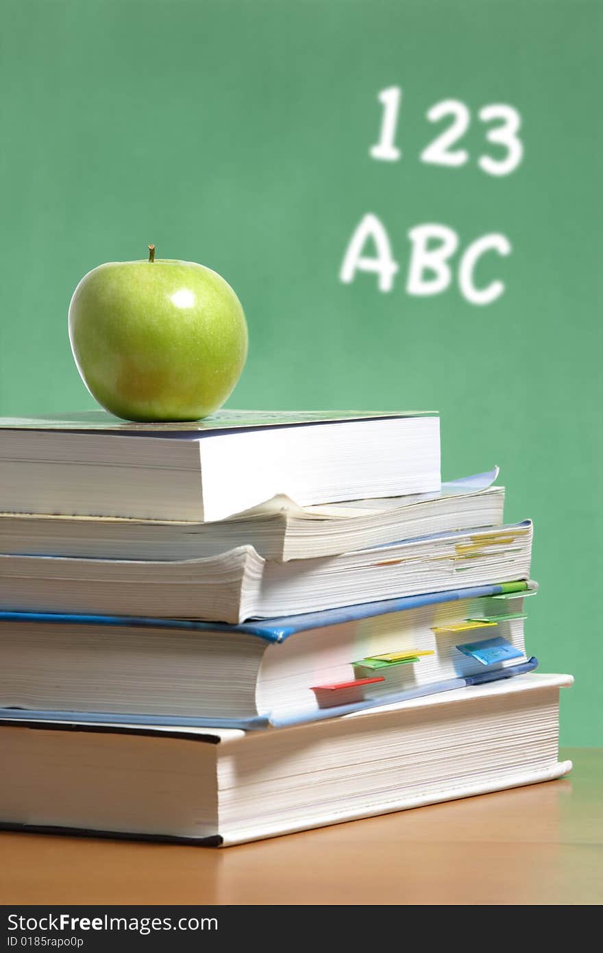 An apple on a stack of books on the teachers desk. An apple on a stack of books on the teachers desk