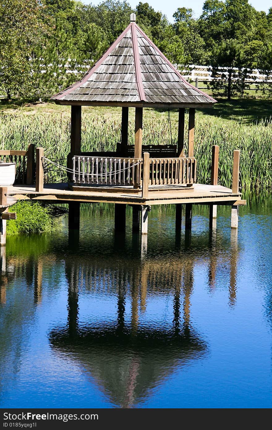Gazebo with wooden shingles at pond with blue reflection. Gazebo with wooden shingles at pond with blue reflection