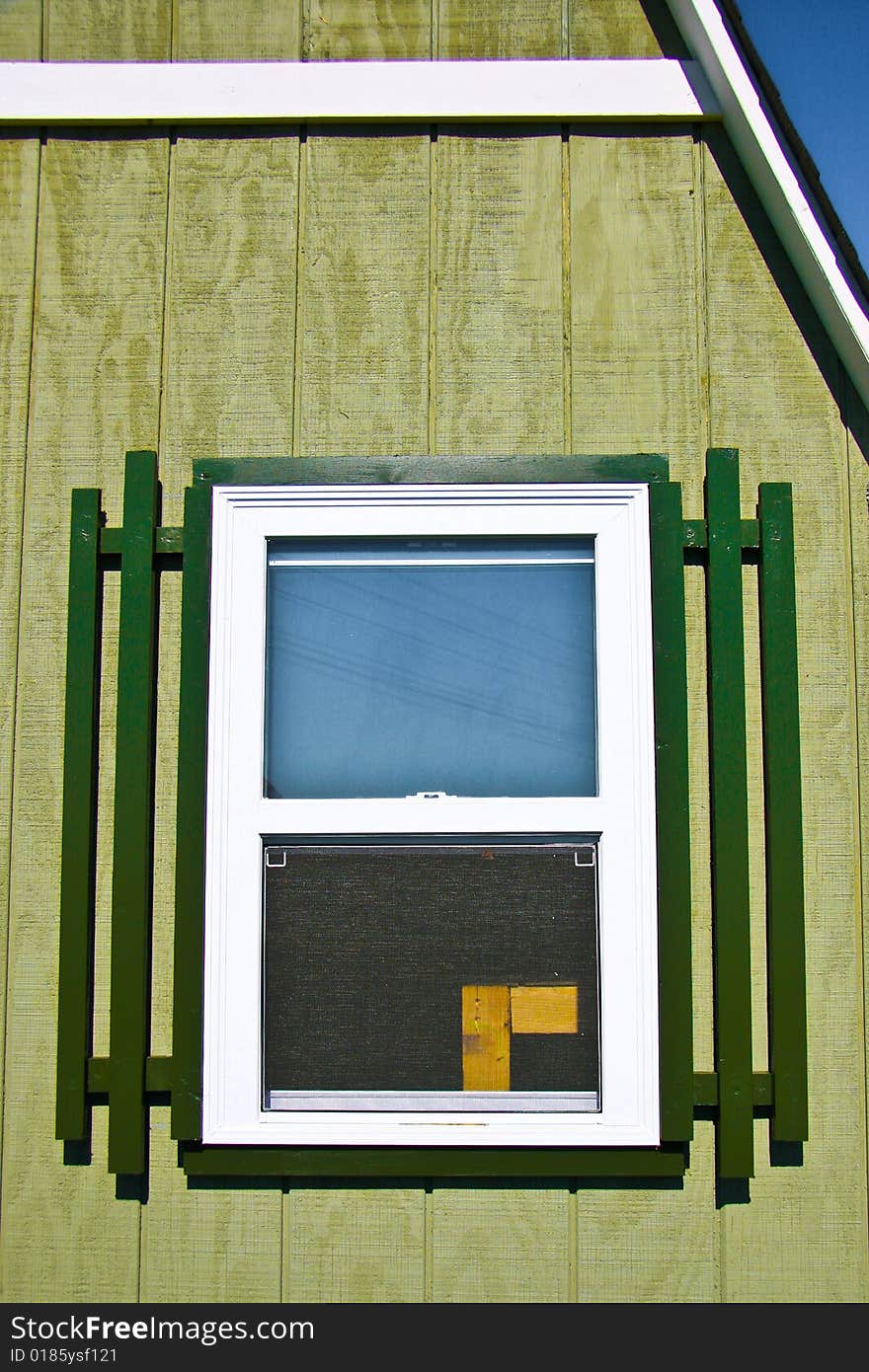 Barn window with green frame and green wall and blue sky