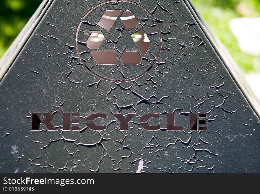 Recycle word and symbol cut out of metal with outdoor stret scene in background. Recycle word and symbol cut out of metal with outdoor stret scene in background