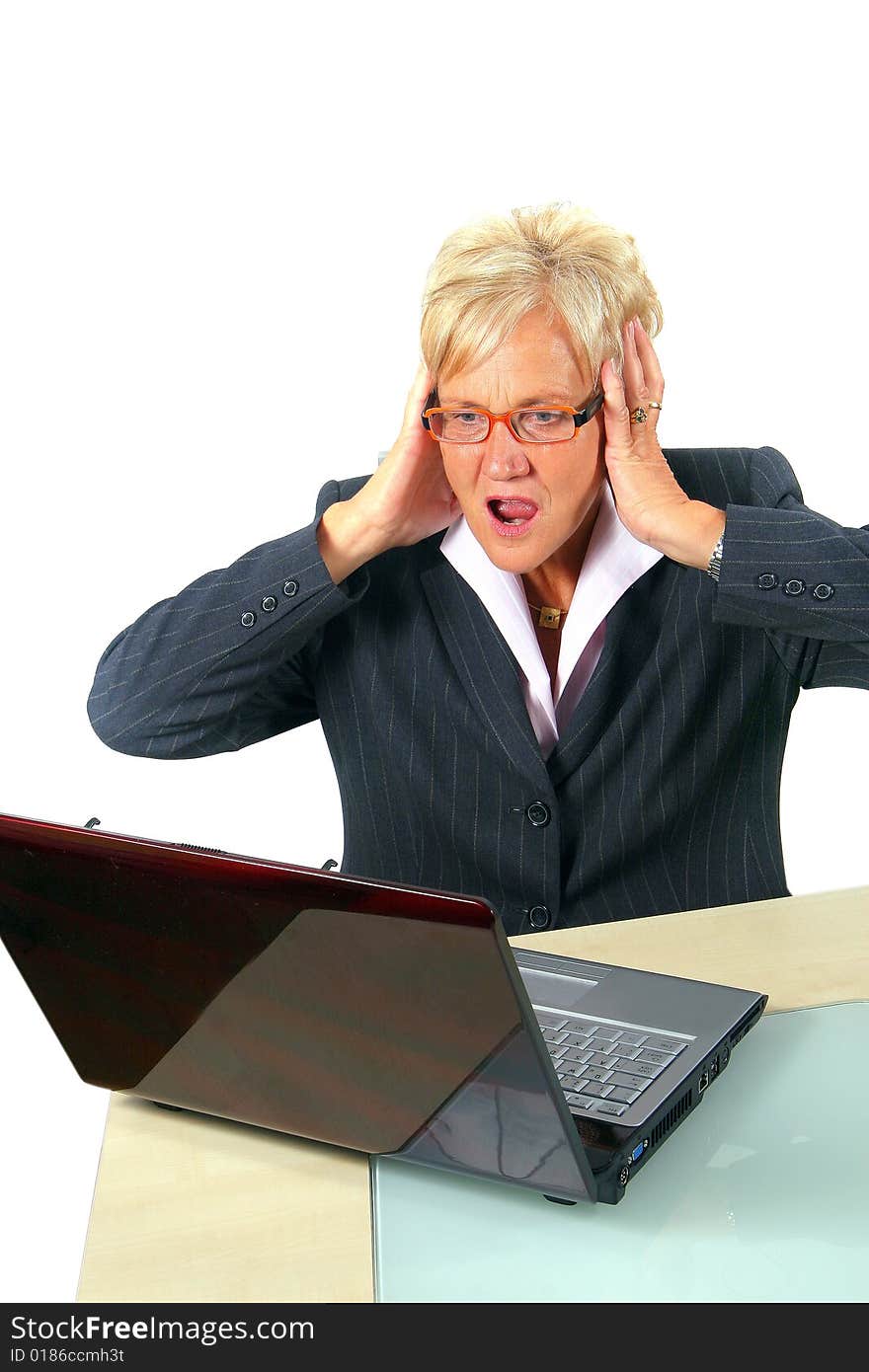 A businesswoman in her sixties in front of a laptop shocked with her hands on her head. Isolated over white. A businesswoman in her sixties in front of a laptop shocked with her hands on her head. Isolated over white.