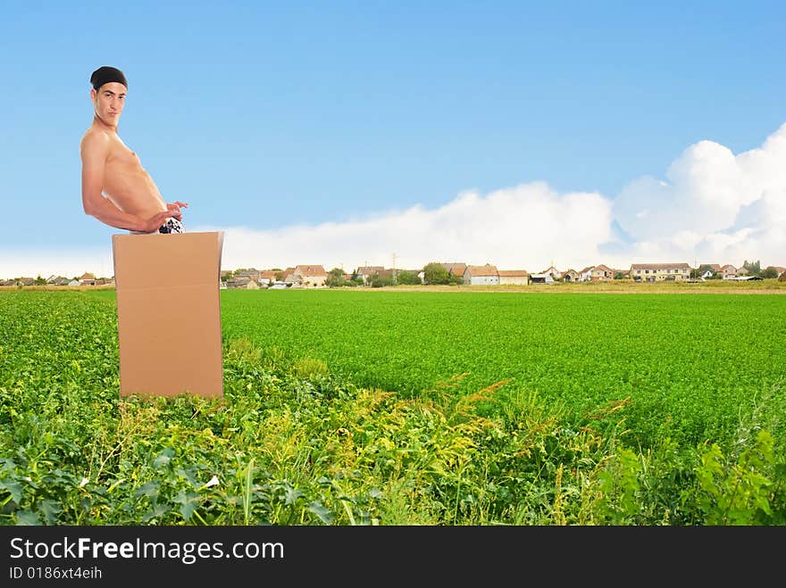 Young man in carton at level field with village on horizon. Young man in carton at level field with village on horizon