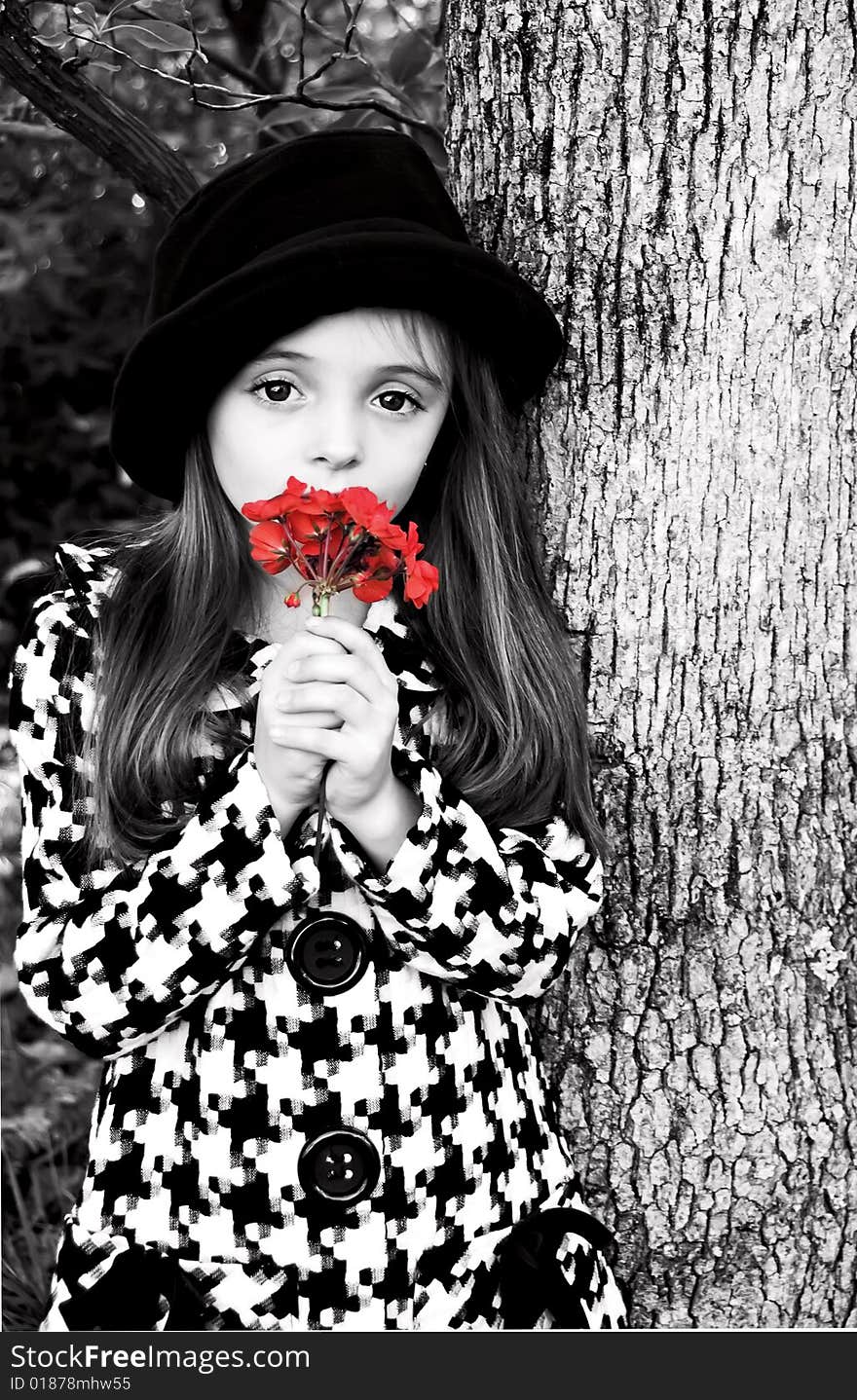 Little girl standing by a tree wearing a coat and hat holding a flower. Little girl standing by a tree wearing a coat and hat holding a flower.