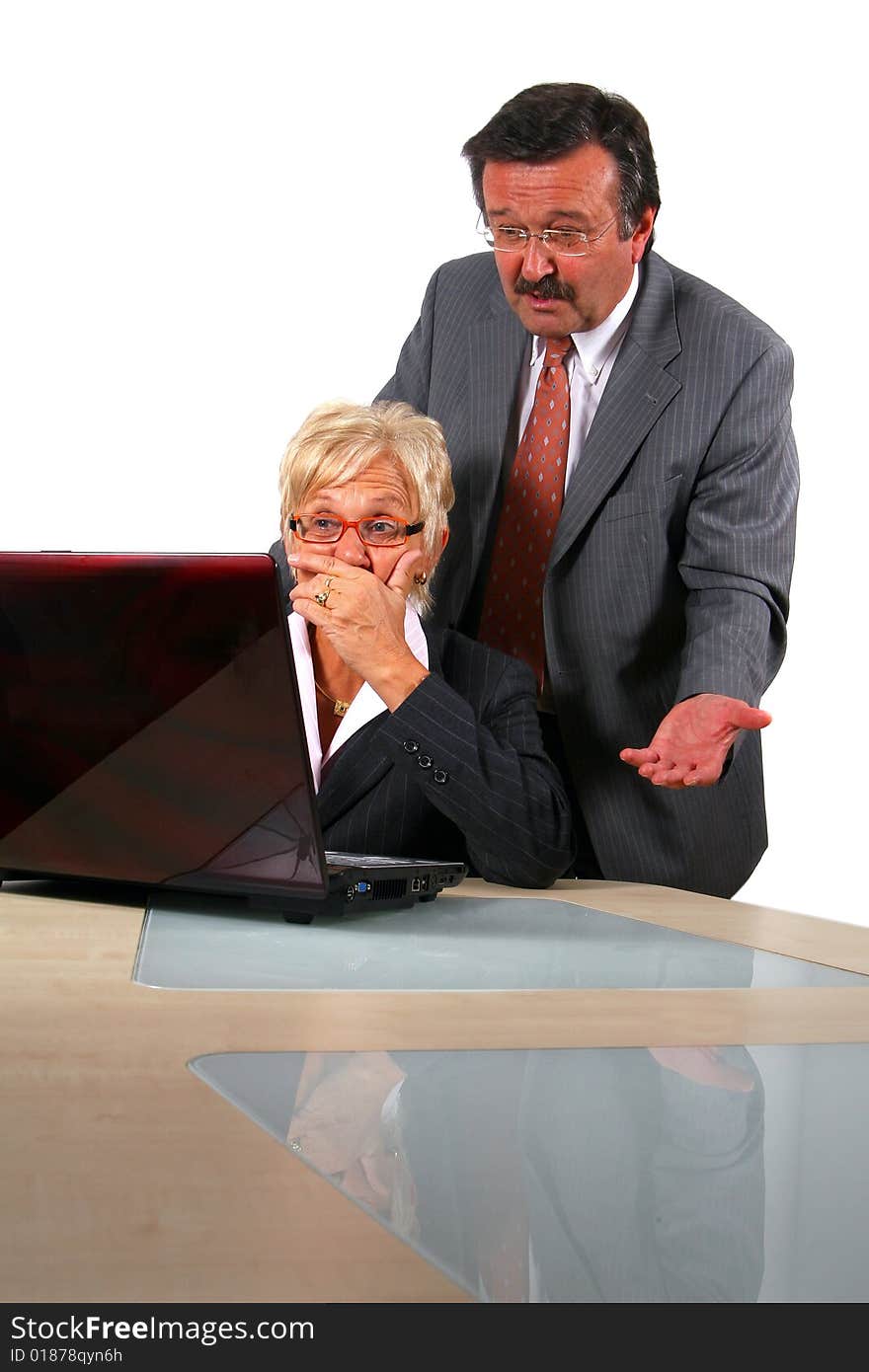 A business woman and a man in front of a laptop on a desk. The man explains something to the woman. She is shocked. Isolated over white. A business woman and a man in front of a laptop on a desk. The man explains something to the woman. She is shocked. Isolated over white.