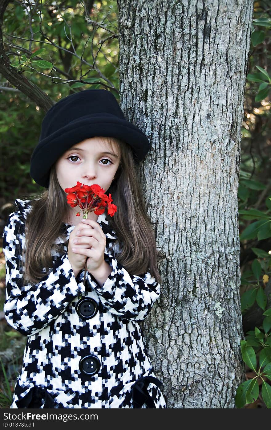 Little girl standing by a tree wearing a coat and hat holding a flower. Little girl standing by a tree wearing a coat and hat holding a flower.