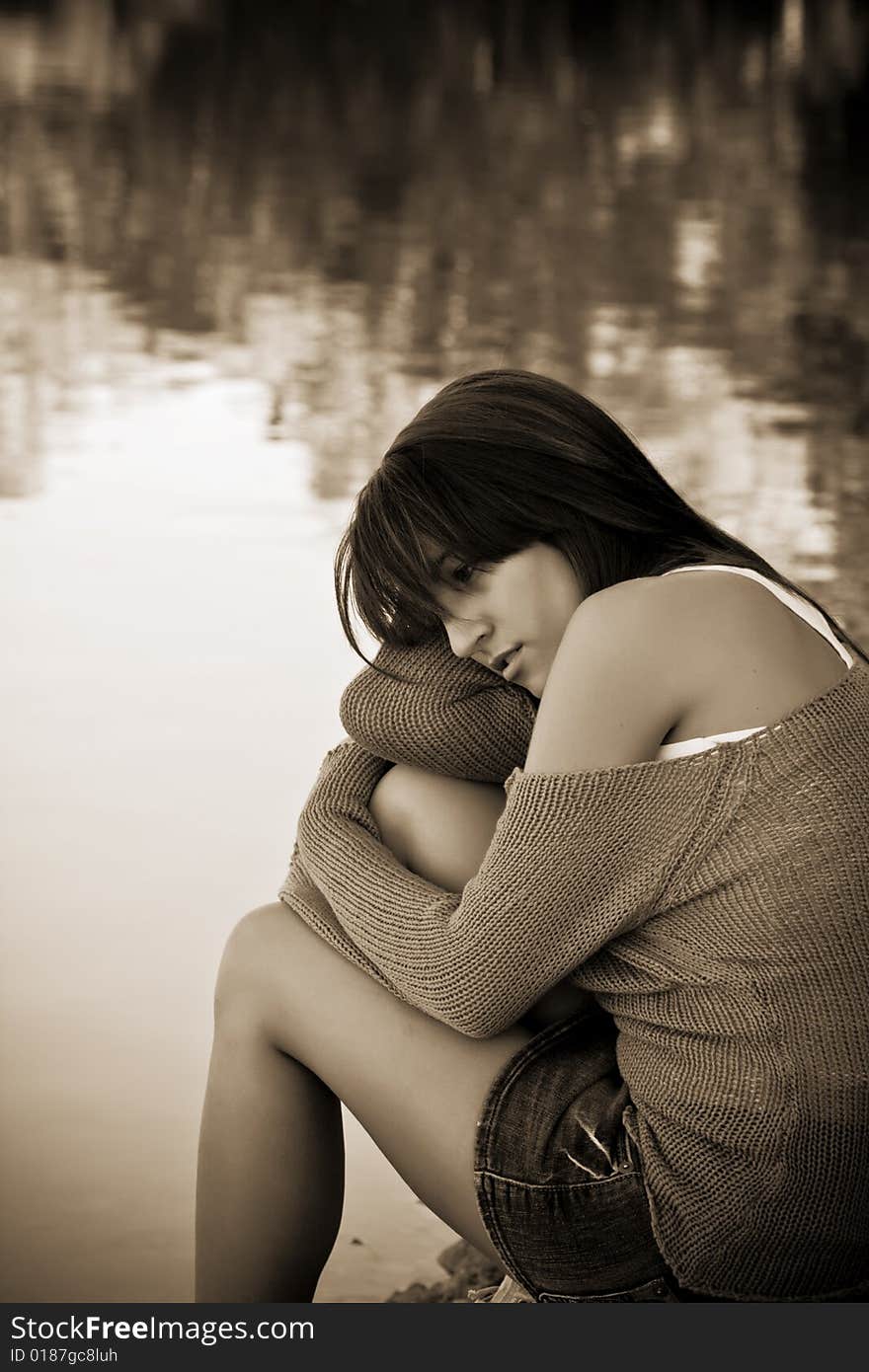 Young thoughtful woman against water background. Sepia toned.