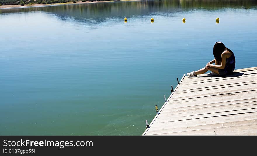 Young woman sitting in a pier in a lake. Young woman sitting in a pier in a lake.