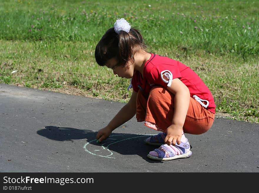 Little girl is drawing on asphalt