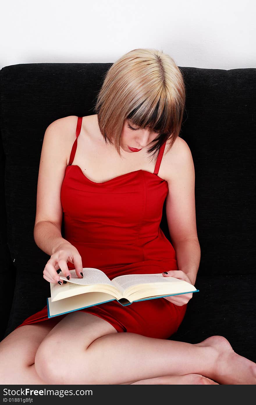 Beautiful blond girl in red dress reading a book