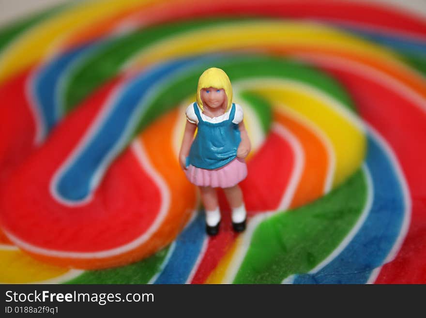 A miniature girl figure stands on top of a giant sucker or lollipop. A miniature girl figure stands on top of a giant sucker or lollipop.