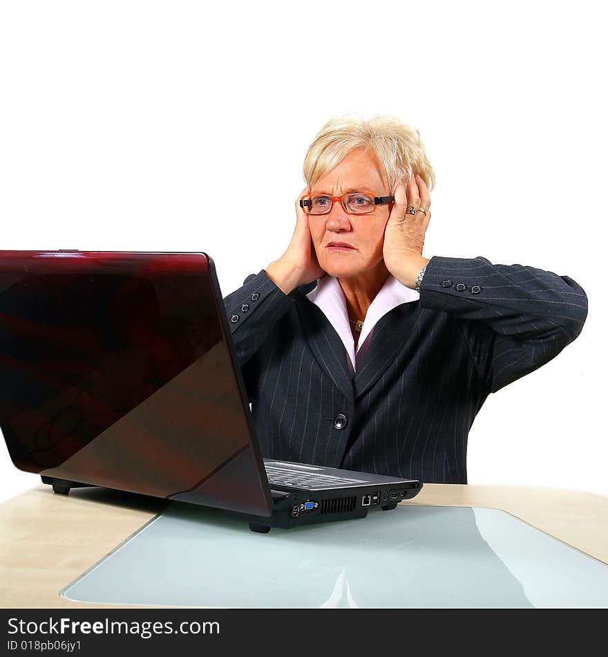 A businesswoman in her sixties in front of a laptop shocked with her hands on her head. Isolated over white. A businesswoman in her sixties in front of a laptop shocked with her hands on her head. Isolated over white.