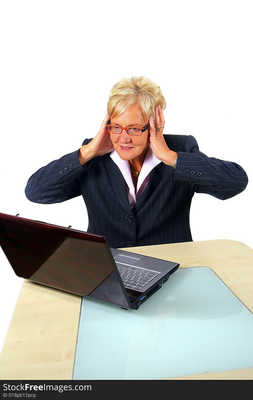 A businesswoman in her sixties in front of a laptop shocked with her hands on her head. Isolated over white. A businesswoman in her sixties in front of a laptop shocked with her hands on her head. Isolated over white.