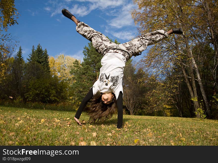 A young woman makes a handstand on grass in front of blue sky