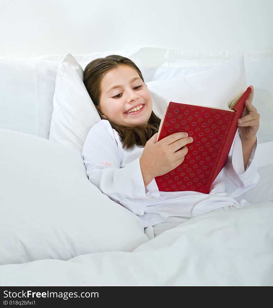 Young girl lying in bed and reading a red book. Young girl lying in bed and reading a red book