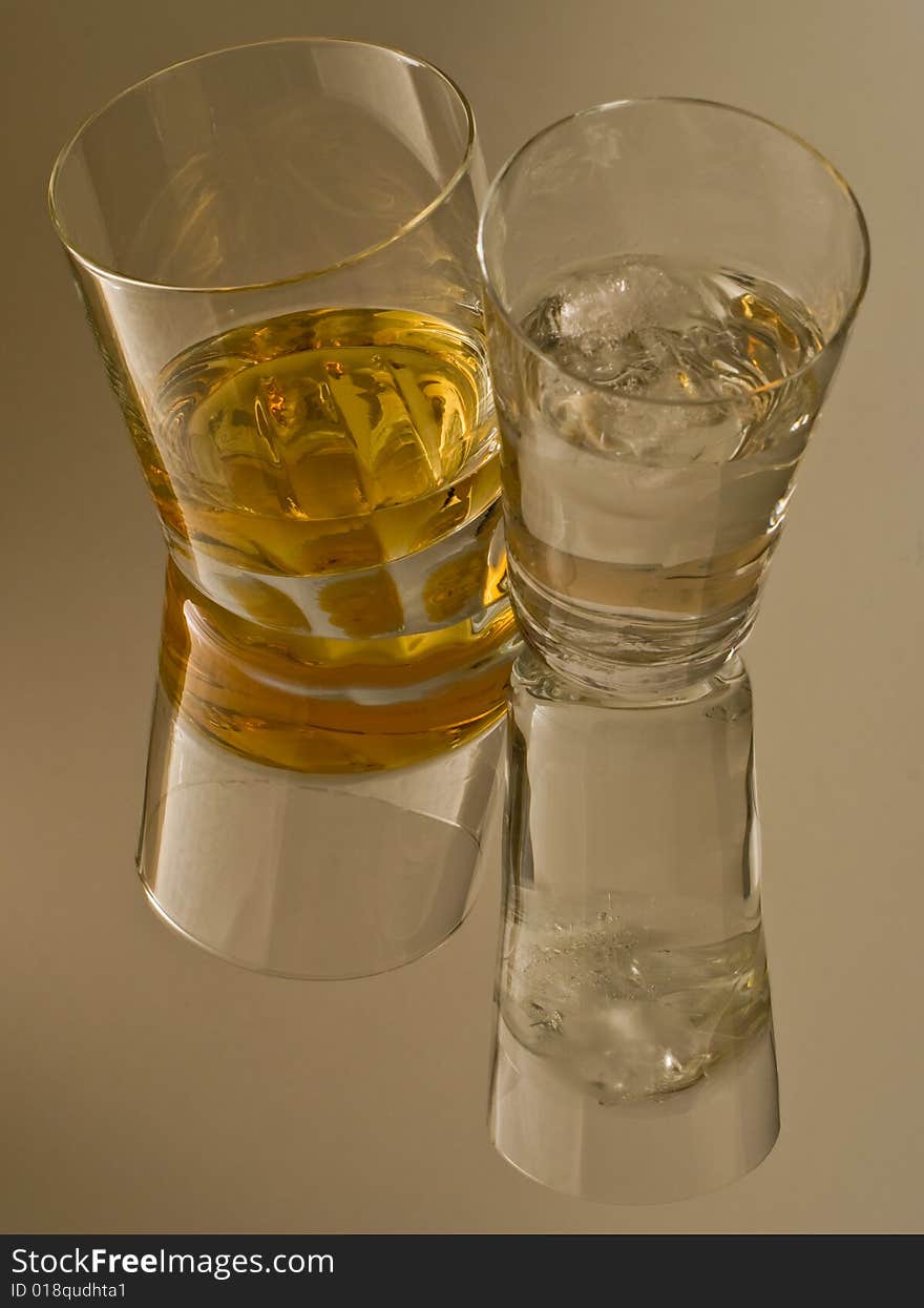 A glass of whiskey and a glass of ice water reflected in the surface. A glass of whiskey and a glass of ice water reflected in the surface.