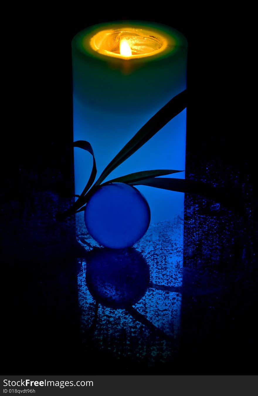 A blue candle and a transparent glass sphere against a black background.