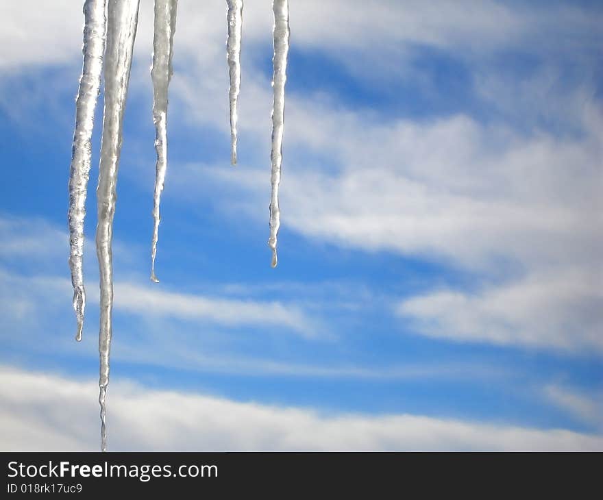 Icicles against a blue sky with clouds.