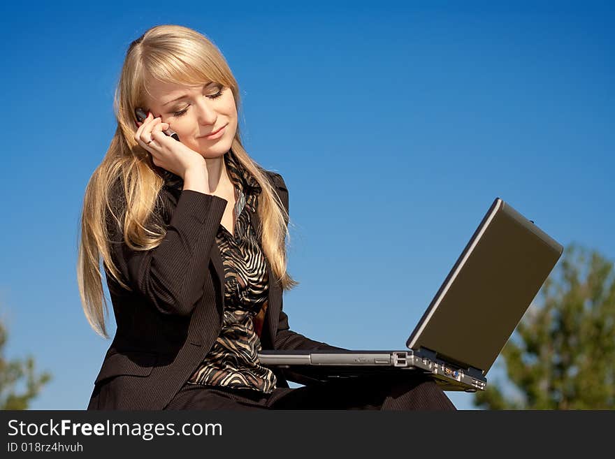 Young blonde business woman working on laptop computer and talking on cell phone. Young blonde business woman working on laptop computer and talking on cell phone