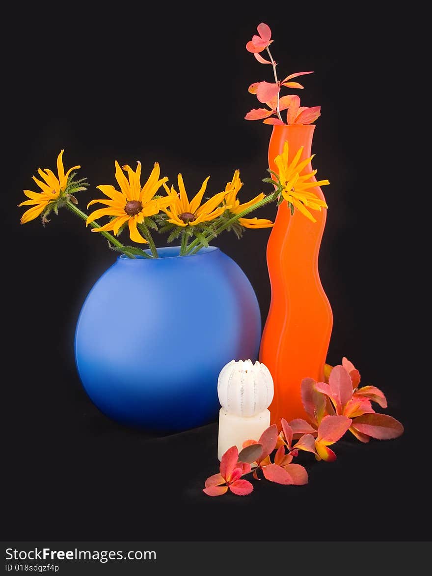 Camomiles yellow in blue vase on black background with an autumn branch and decorative burning candle. Camomiles yellow in blue vase on black background with an autumn branch and decorative burning candle