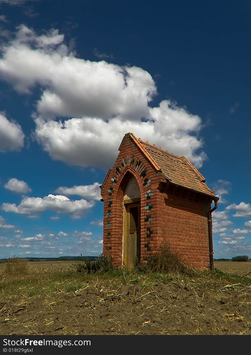 Village chapel in the middle of wide field and blue sky